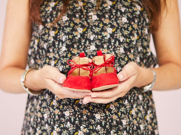 Expecting mother holding red shoes for baby