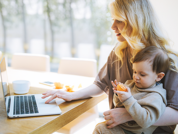 Parent holding baby while working on laptop